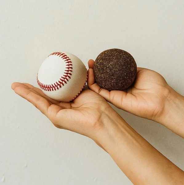 Mano sosteniendo una pelota de béisbol y una pelota creada con sargazo